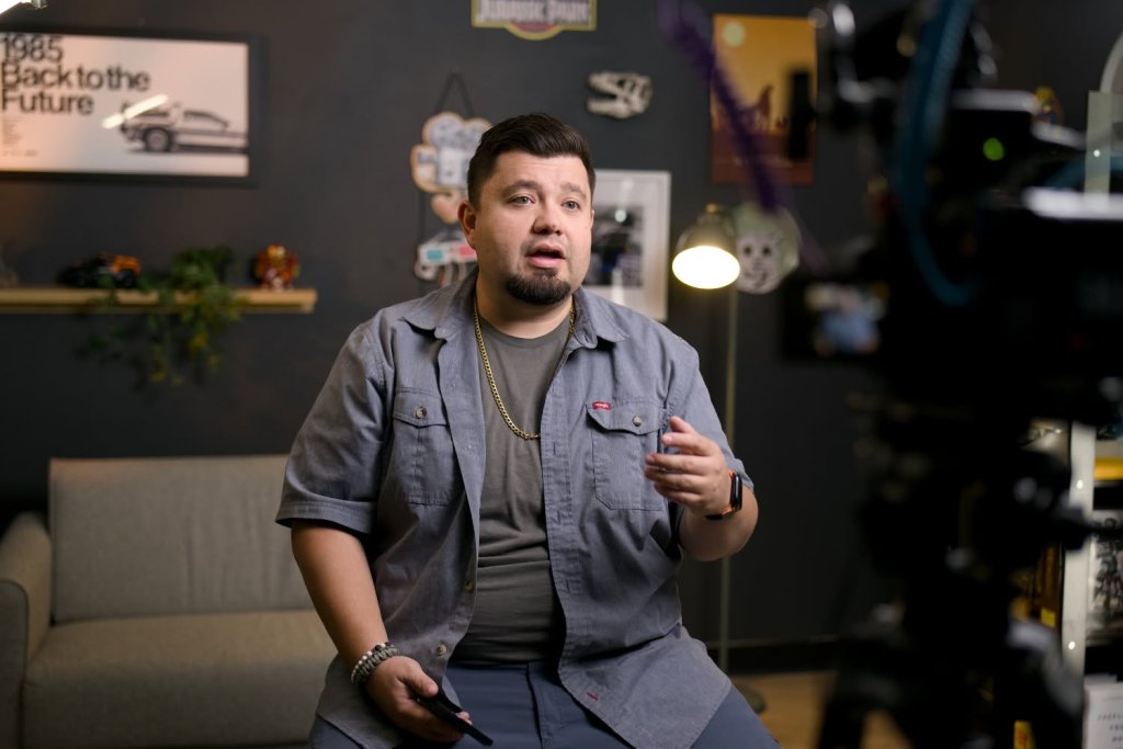 Danny talking to camera in his studio, with a Back to the Future poster and a lamp behind him.