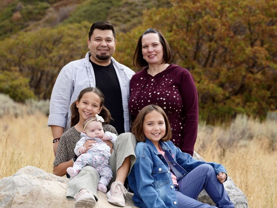 Danny, his wife and their daughters sitting together on a large boulder in front of an autumn mountainside.